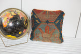 Antique Caucasian rug pillow displaying distressed geometric patterns in blue and terracotta, tangerine velvet edge.