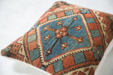 Angled close-up of faded red and blue geometric motif on antique Caucasian rug fragment pillow.