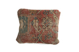 Corner detail of antique Heriz rug fragment pillow, showing visible wear and red, beige, blue geometric pattern.