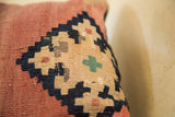Close-up of antique Kilim pillow's geometric weave, featuring faded beige, dark blue, and rust tones.