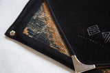 Rug fragment clutch corner showing the black suede lining and Swag and Tassel brand logo.
