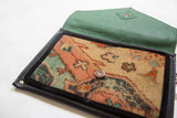 Handmade Rug Fragment Clutch with a patterned woven front, black trim, and green leather flap.