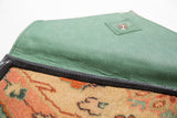 Rich green vegetable suede lining and metal snap closure of the handmade rug fragment clutch.