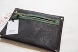 The black vegetable suede back of the clutch with its green zipper and tassel tag.