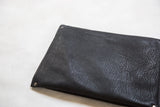 Handmade clutch back showing black textured vegetable suede and metal rivets.