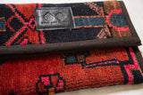 Handmade rug fragment clutch, Swag and Tassel label on richly textured red, black, fuchsia geometric pattern.
