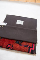Open rug clutch revealing dark interior lining, Swag and Tassel label, and red geometric fragment.