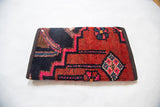 Hand-knotted rug fragment clutch detail, showcasing tribal geometric pattern in red, navy, and pink.