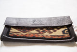Textured dark leather flap, Swag and Tassel logo, and geometric rug fragment.