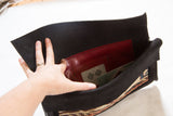 Interior of rug fragment clutch, featuring a hand, rich red pocket, and brand label.