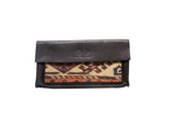 Textured dark leather flap with embossed logo and geometric rug fragment on handmade clutch.