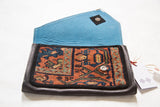 Handmade rug clutch showing the bright blue vegetable suede lining and snap closure.