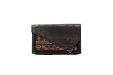 Handmade rug fragment clutch with a dark brown suede flap over a colorful geometric textile.