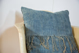 African Indigo pillow's sun-faded blue textile, vertical stripes, and handcrafted natural fringe.