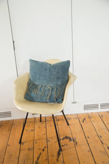 African Indigo pillow, sun-faded blue textile with woven texture and fringed edge.