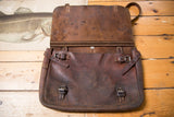Open vintage dark brown leather messenger bag, its aged interior and buckle straps visible.