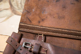 Distressed brown leather texture with pale stitching detail on the messenger bag.
