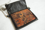 Antique Kurdish rug fragment on black leather, featuring geometric orange and blue patterns.