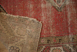 Vintage Malayer rug's folded corner, revealing worn red pile, visible foundation, and tattered fringe.