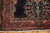 Fine Sarouk rug corner with a rich raspberry red border, dark indigo field, and short ivory fringe.