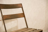 Close-up of vintage French cafe chair's weathered wood backrest and metal frame patina.