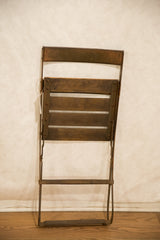 Folded vintage French cafe chair, highlighting aged metal frame and wood slats.