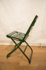 Angled side view of vintage French cafe folding chair, dark green patina.
