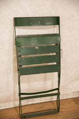 Folded vintage French cafe chair, showing aged green metal and wood slats.
