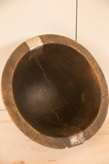 Dark wood interior of a vintage African bowl with visible crack repairs and carved rim.