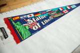 Detailed graphic of the Statue of Liberty and international flags on a blue vintage felt pennant.