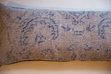 Detail of vintage Turkish rug fragment pillow, distressed blue curvilinear pattern on beige.