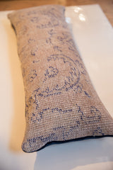 Close-up of Reclaimed Rug Fragment Pillow, textured beige with deep blue patterns, navy velvet edge.