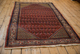 Angled view of a vintage Arak Sarouk rug showcasing its red field, navy border, and copper-green spandrels.