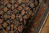 Fine weave and dense pile of a folded antique Serapi rug with a navy Herati motif.