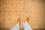 Low pile texture on a distressed Oushak rug in pale gold and faded cochineal red.