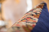 Pillow side detail: textured vintage rug fragment in tan, red, blue with navy fabric.