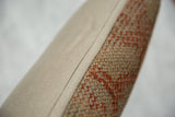 Vintage Turkish rug fragment pillow edge, revealing orange pattern and beige fabric backing.