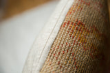 Nubby vintage rug fragment texture with orange, yellow flecks, and light beige backing seam.