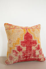 Handmade antique rug fragment pillow with rustic texture and faded red, yellow patterns.
