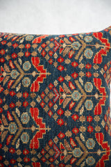 Intricate hand-knotted geometric pattern in deep blue, ruby red, and beige on the throw pillow.