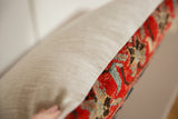 Red, blue patterns and textured light fabric on vintage rug fragment pillow side.