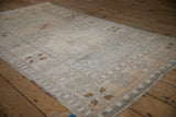 Angled view of a distressed Oushak rug highlighting its wide floral border and silver-ivory tones.