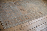 Angled view of a vintage distressed Oushak rug, highlighting its low pile and soft colors.