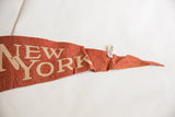 Vintage reddish-brown felt pennant, cream 'NEW YORK' letters, textured fabric, and attached handwritten tag.