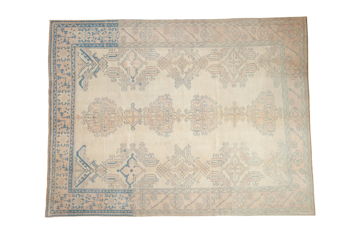 A distressed vintage Oushak rug with oversized palmettes in pale dusty rose and blue on an ivory field.