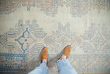 Looking down at the soft, worn texture of a vintage Oushak rug in ivory, rose, and blue.