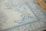 Corner of a distressed Oushak carpet showing low pile texture and sky blue and rose floral motifs.