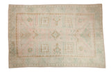 Vintage distressed Oushak carpet with a geometric grid design in soft pink, baby teal-blue, and dusty gold.