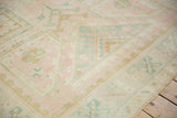Soft-focus detail of faded geometric motifs in pink, dusty gold, and teal on a vintage rug.