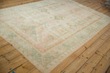 Angled view of the distressed Oushak carpet's geometric pattern in soft pink, teal, and ivory.